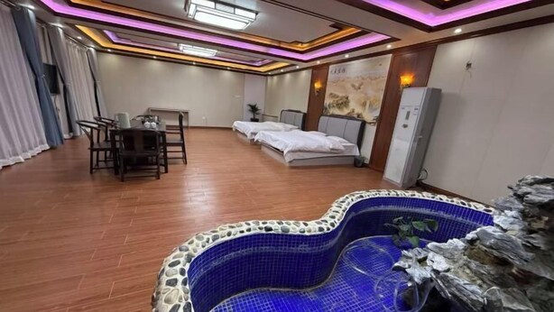 A hotel room with a blue tiled jacuzzi, wooden flooring, a dining area with a table and chairs, and a bed with a headboard. - Haojin Business Hotel (Erenhot)