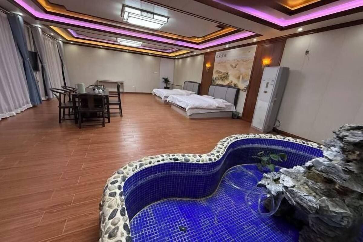 Habitación de hotel con un jacuzzi de azulejos azules, suelo de madera, zona de comedor con mesa y sillas, y una cama con cabecera.