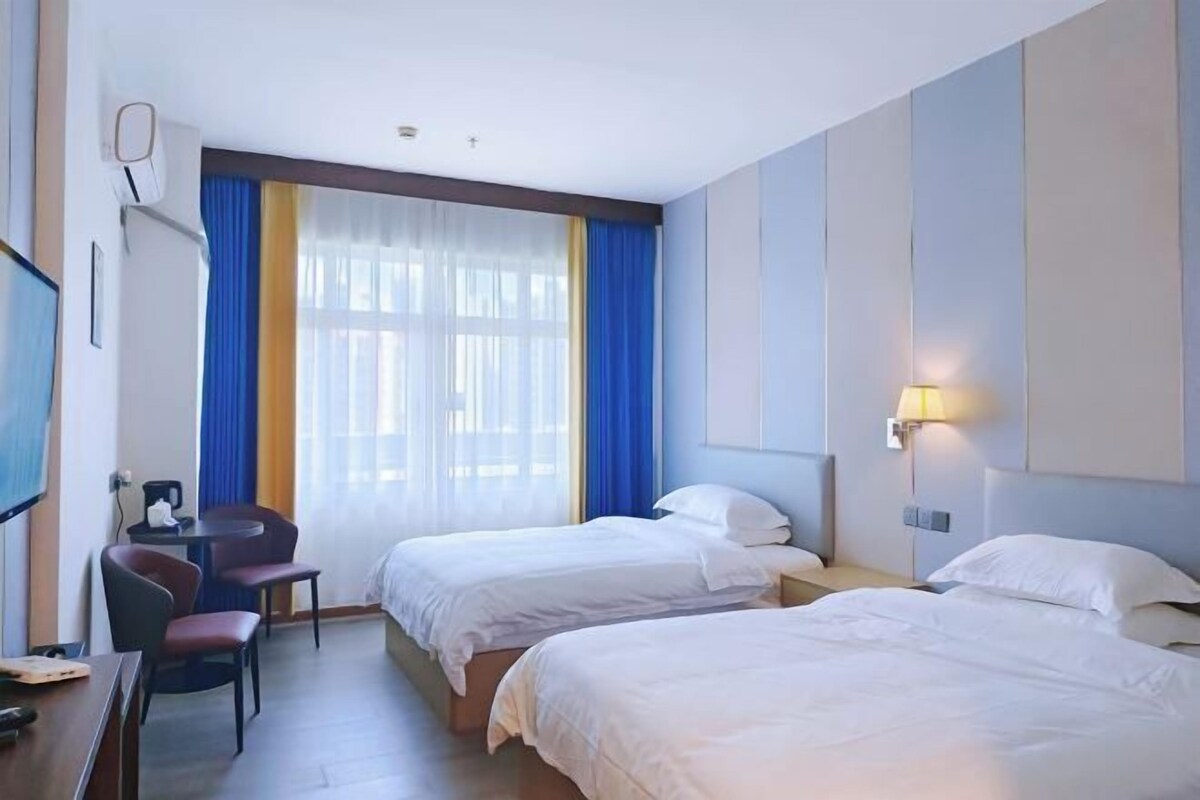 A hotel room with two beds, a desk with a chair, a TV, and a window with curtains.