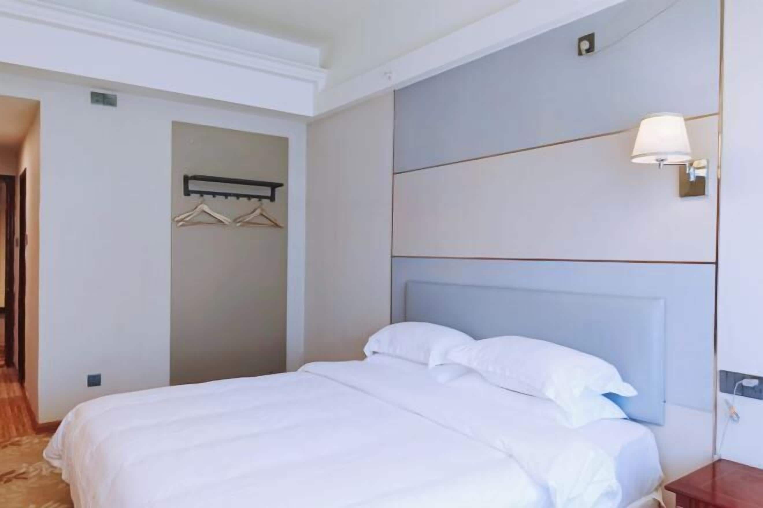 Hotellihuone, jossa on sänky, seinään kiinnitetty valaisin ja naulakko.