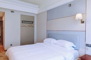 A hotel room with a bed, a wall-mounted lamp, and a coat rack.