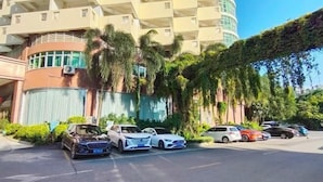 A parking lot with several cars, a building with balconies, and a covered area with plants. - Yaduo Holiday Hotel (Zhongshan)