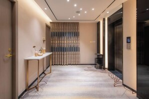 A hotel hallway with a reception desk, a patterned curtain, and an elevator. - Longfeng Hotel (Enping)