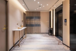 Un pasillo de hotel con una mesa de recepción, una cortina estampada y un ascensor.