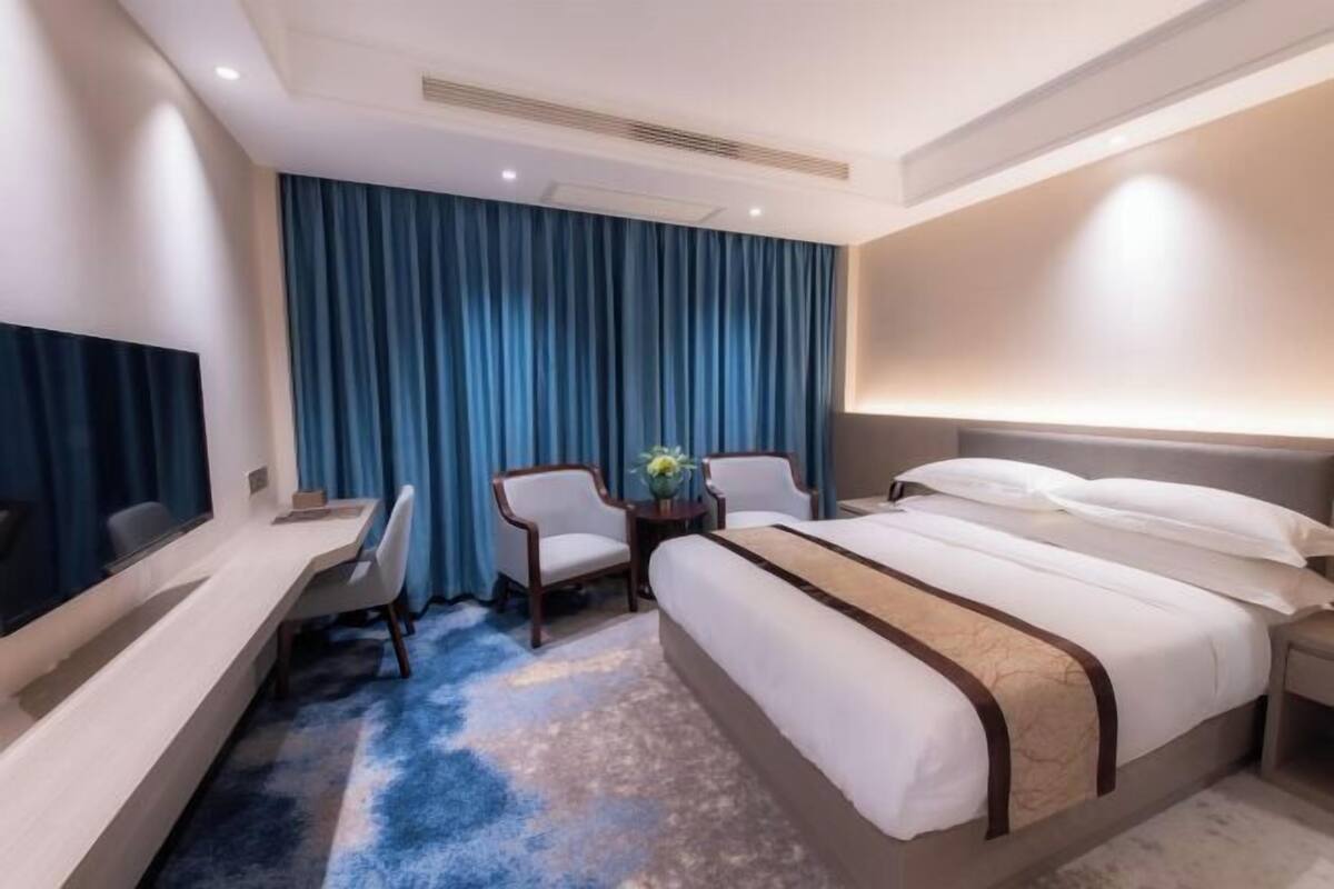 A hotel room with a bed, a desk, a chair, a TV, and a large window with curtains.