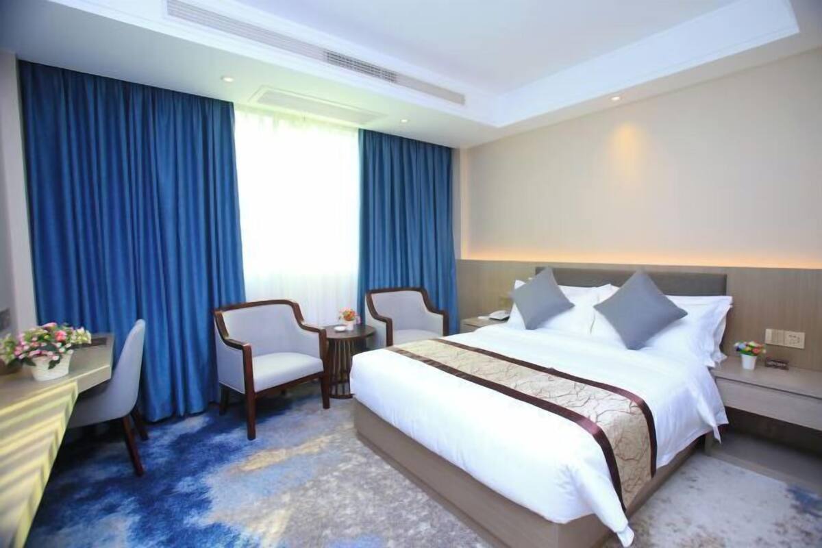 A hotel room with a large bed, two armchairs, a desk with a lamp, and a small table with flowers.