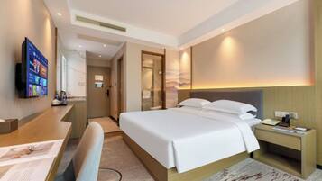 A hotel room with a bed, bedside table, desk, chair, and a television.