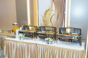 Una mesa de buffet con diversas opciones de comida, un dispensador de bebidas y un fondo decorativo.