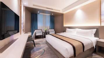 A modern hotel room with a large bed, a desk, a TV, and a seating area with a table and chairs.