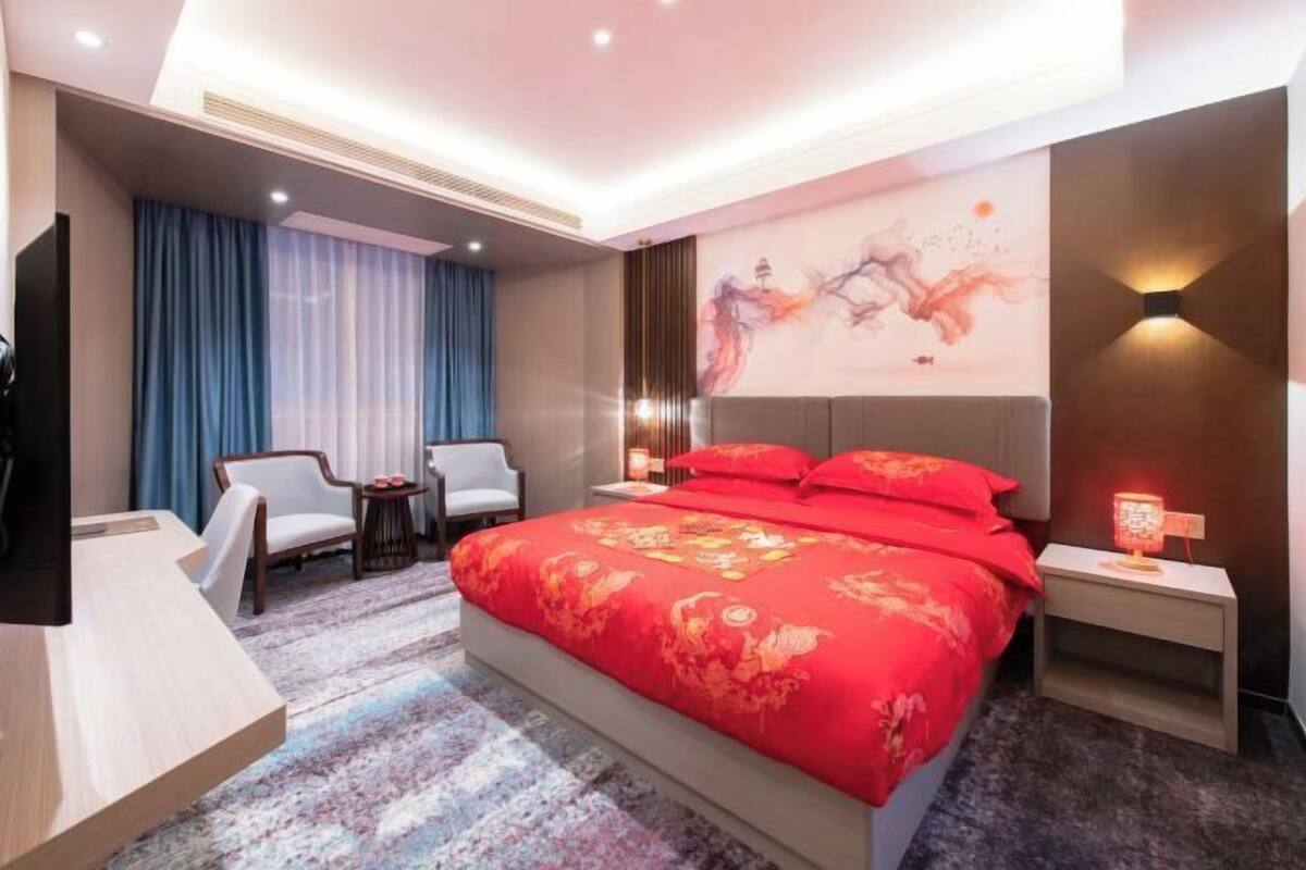 A hotel room with a large bed, two bedside tables, a TV, a desk, and a chair.
