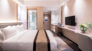 Habitación de hotel con cama, escritorio, televisor y baño visible a través de una puerta abierta.