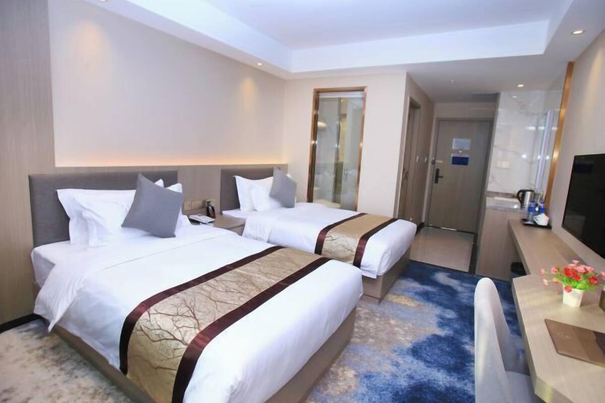 A hotel room with two beds, a desk, a TV, and a bathroom door.