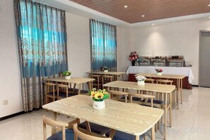 A dining area with multiple tables and chairs, a kitchen area with buffet setup, and a door leading to another room. - Longfeng Hotel (Enping)