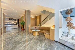 Un moderno vestíbulo de hotel con un mostrador de recepción, una zona de estar curvo, una escalera y una gran obra de arte en la pared.