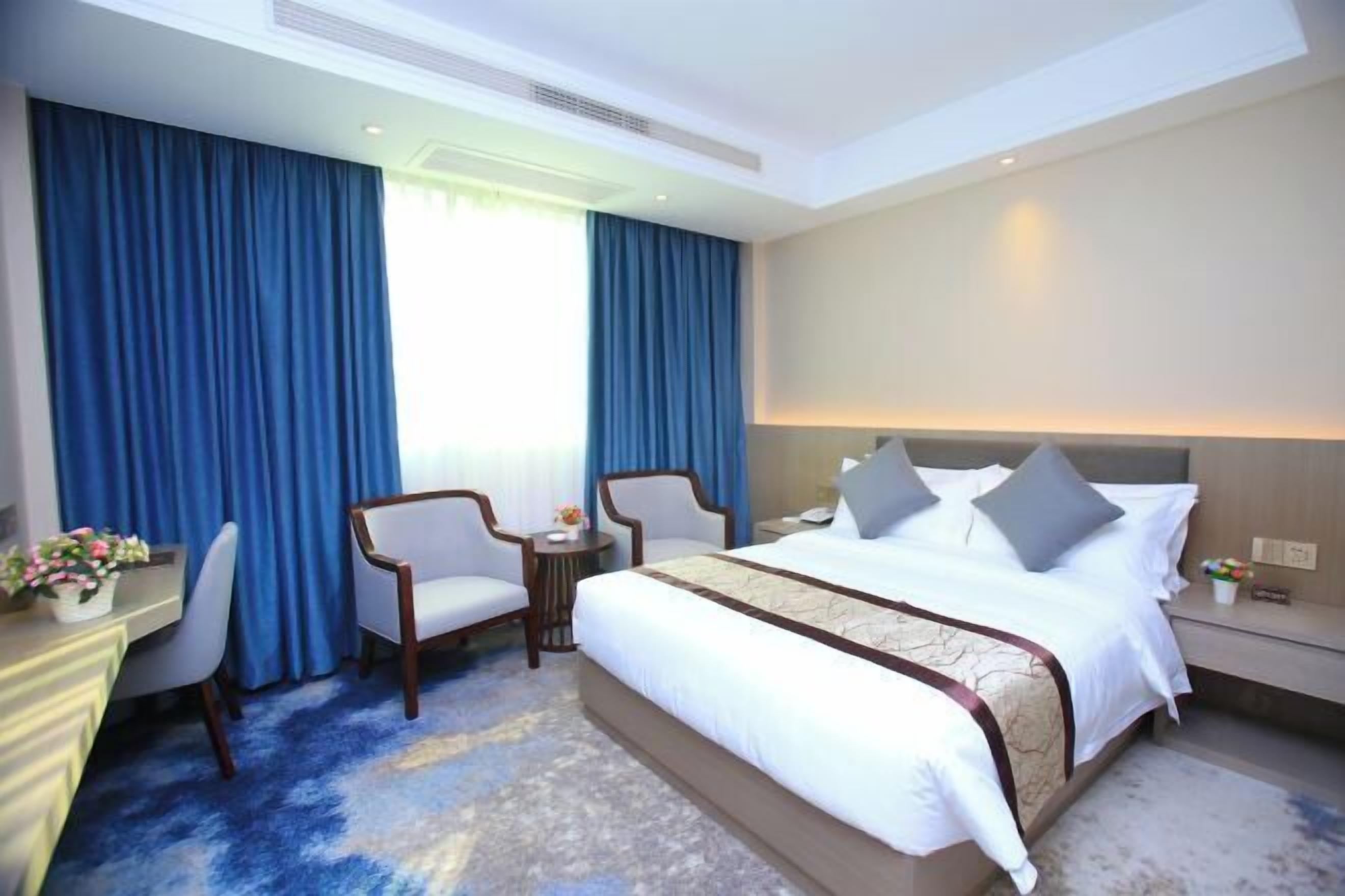 A hotel room with a large bed, two chairs, a desk, and a small table.