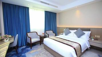 A hotel room with a large bed, two chairs, a desk, and a small table.