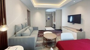 Una habitación de hotel moderna con sofá, una mesita redonda, televisión y escritorio.