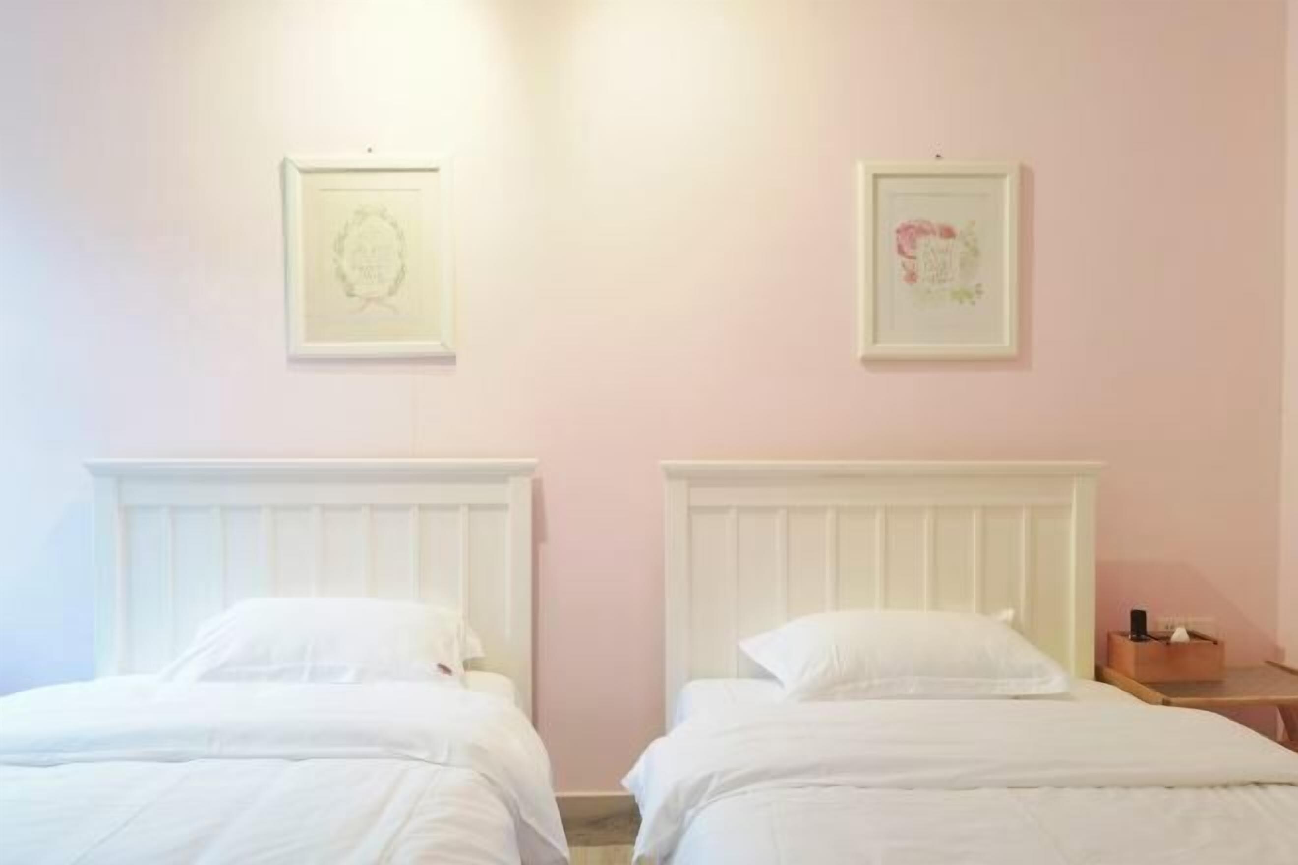 Une chambre avec deux lits, chacun doté d’une tête de lit blanche et de linge de lit blanc. Des tableaux encadrés sont accrochés au mur au-dessus des lits.