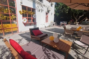Une terrasse extérieure avec des sièges, une table et un bâtiment dont la fenêtre est décorée de ballons et d’une pancarte indiquant « ANNIVERSAIRE ».