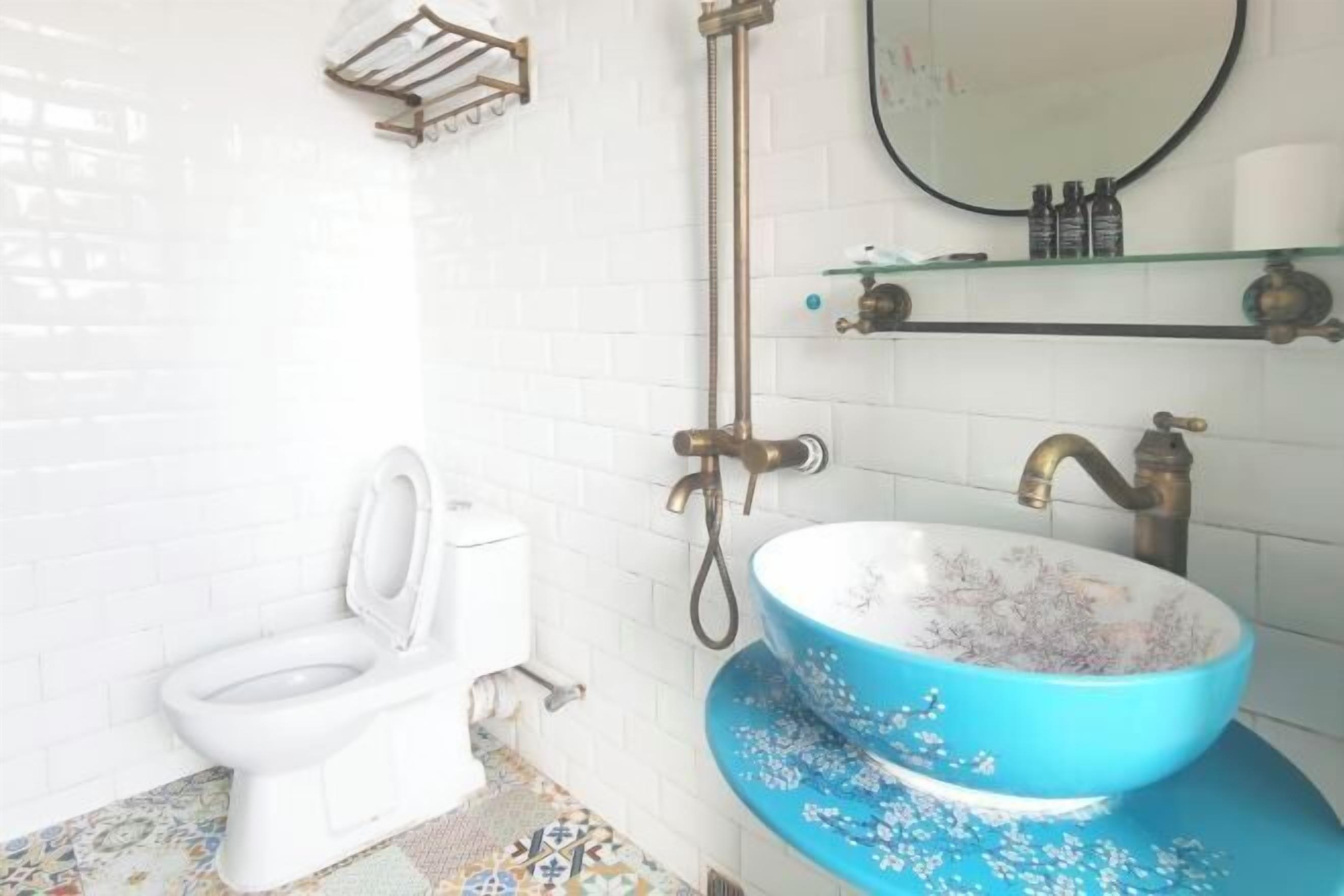 Une salle de bain avec des toilettes blanches, un lavabo en céramique bleue et une douche dotée d’un robinet en laiton.
