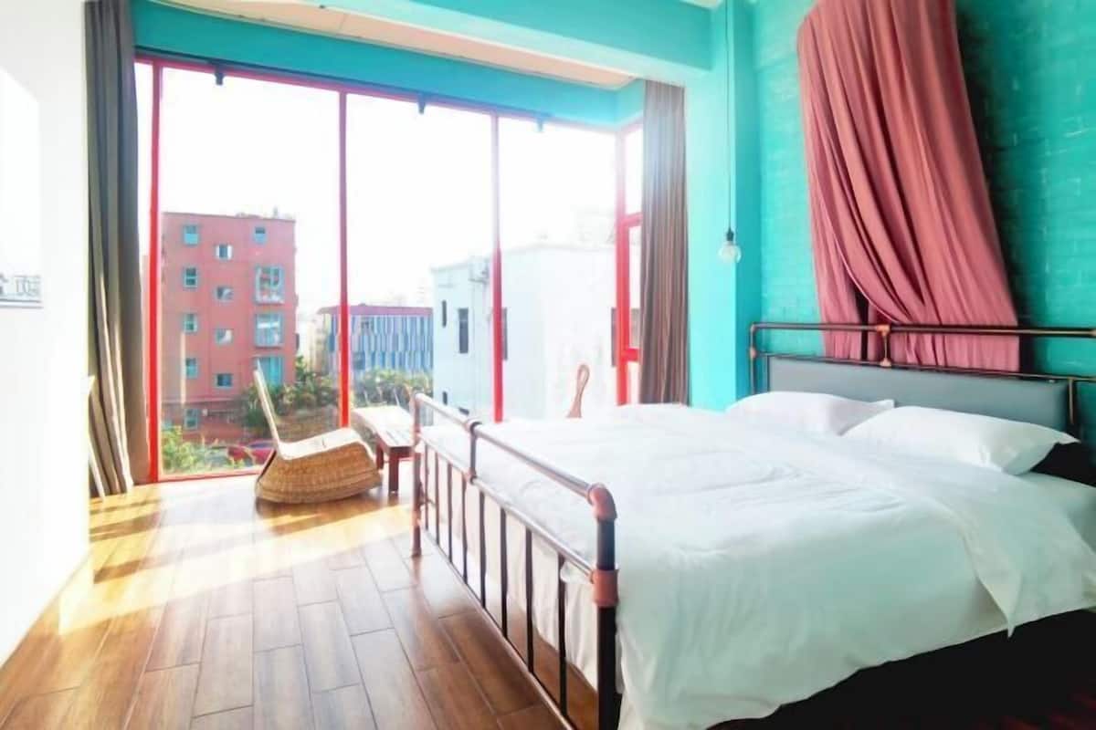 A bedroom with a bed, a chair, and a view of buildings outside.