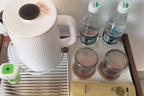 Une bouilloire blanche, deux bouteilles d’eau, deux verres contenant une substance brune, un multiprise vert et une brochure d’hôtel.