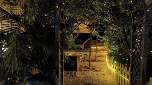 A nighttime view of a garden area with a wooden pergola, string lights, and a small building with a balcony. - XUQIANFENG (Shenzhen)