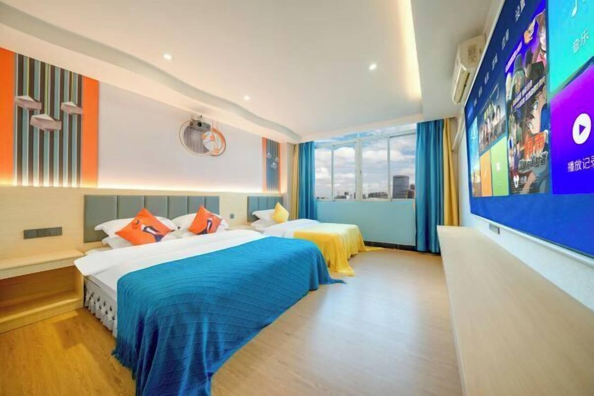 Hotelkamer met twee bedden, een groot raam met uitzicht over de stad en een aan de muur bevestigde televisie die verschillende zenders toont.