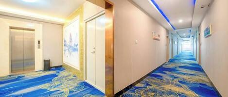 A hotel corridor with a patterned carpet, doors, and a long hallway.