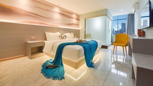 A modern hotel room with a large bed, a desk, a chair, and a view of the city. - Haixing Business Hotel (Zhongshan)