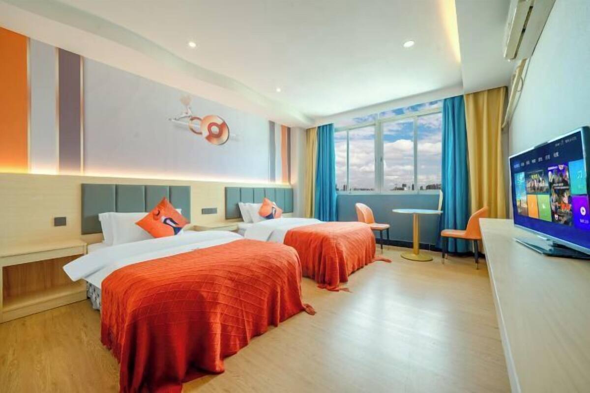 Een hotelkamer met twee bedden, een televisie, een bureau en een raam met gordijnen.