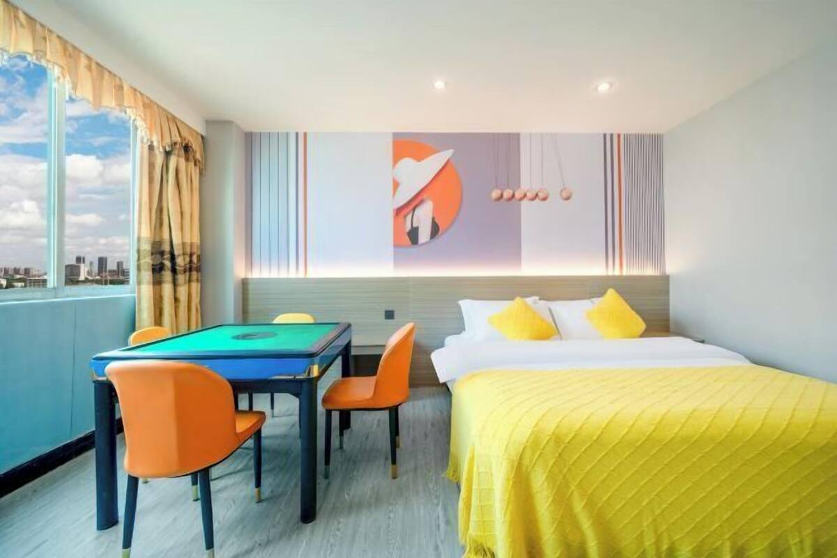 Een hotelkamer met een pooltafel, een bed met geel beddengoed en uitzicht op de stad.