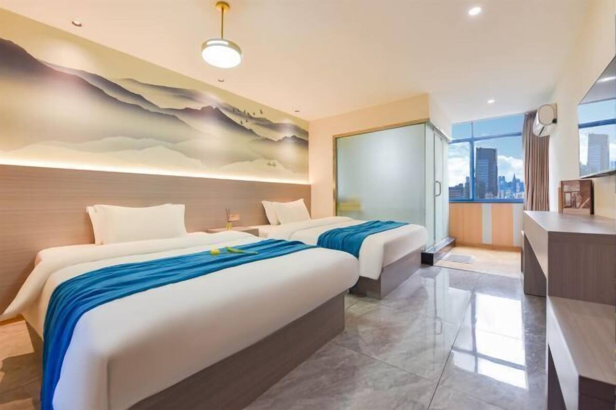 Een moderne hotelkamer met twee bedden, uitzicht over de stad, een bureau en een decoratief muurschildering.