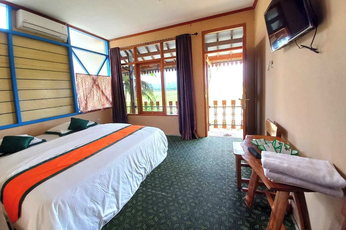Une chambre d’hôtel avec un lit, un bureau, une télévision et un balcon offrant une vue.