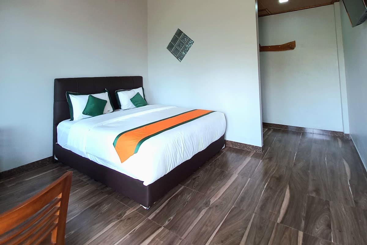 Une chambre avec un plafond en bois, un lit avec une literie blanche et des coussins verts, un plancher en bois et une petite chaise en bois.