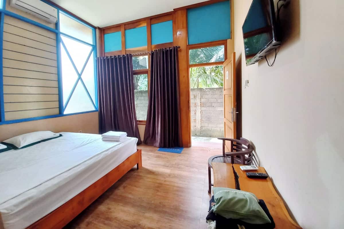 Une chambre à coucher avec un lit, un bureau, une chaise, un téléviseur et une fenêtre avec des rideaux.