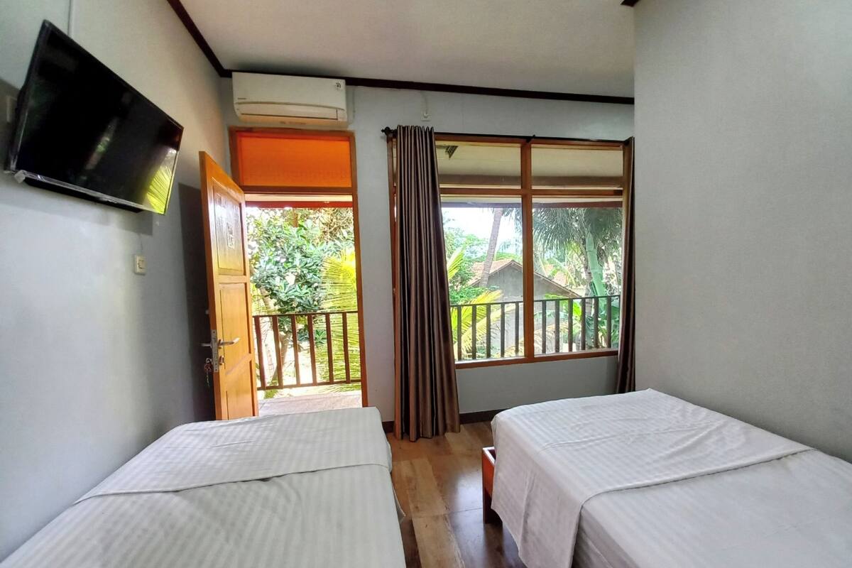 Une chambre dotée de deux lits, d’un appareil de climatisation, d’une télévision, d’un balcon offrant une vue sur la verdure et d’une porte donnant sur l’extérieur.