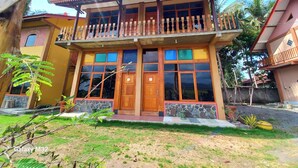 Une maison à deux étages dotée d’un balcon, de grandes fenêtres et de fondations en pierre.