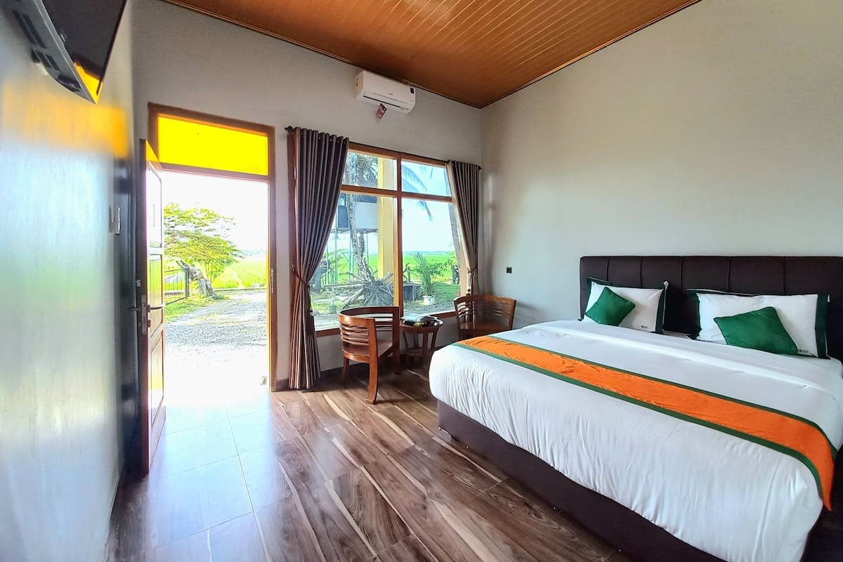 Une chambre d’hôtel avec un grand lit, un plancher en bois, une fenêtre avec des rideaux et un appareil de climatisation fixé au plafond.