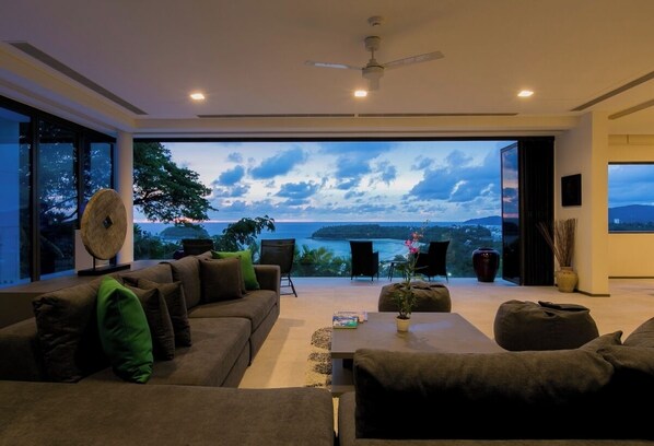 Una sala de estar moderna con un ventanal grande que ofrece una vista panorámica del océano y las colinas.