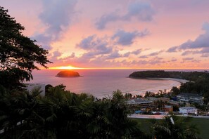 A coastal sunset view with a beach, palm trees, and buildings in the foreground. - The Heights Penthouse A5 3Bedrooms Seaview near Kata Beach (Muang)