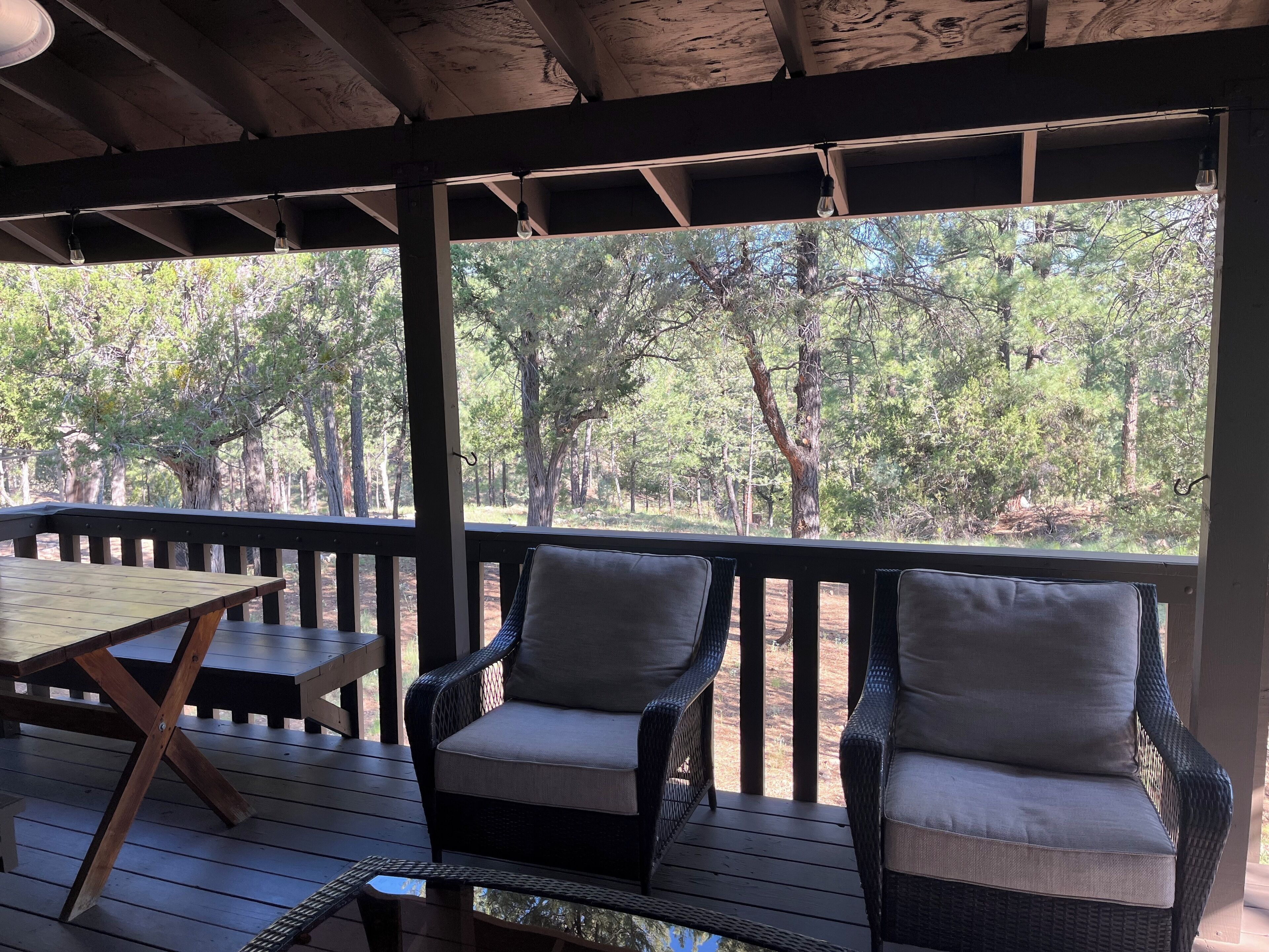 A covered outdoor area with a wooden table and two wicker chairs.