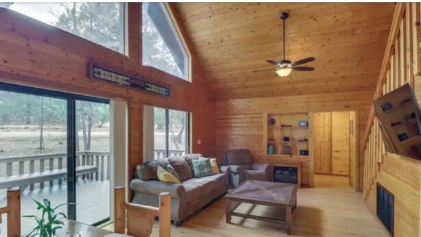 A spacious wooden cabin with a large sliding glass door, a ceiling fan, a sofa, a coffee table, and a fireplace. - Happy cabin in Heber (Heber)