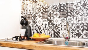 Una cocina con salpicadero decorado, una cafetera, un frutero y un lavabo.