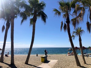 Ein Strand mit Palmen, einer Holzpromenade und Menschen, die am Wasser entspannen.