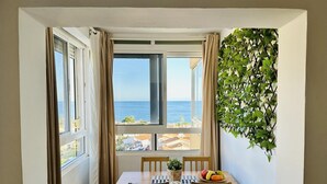 A dining area with a table and chairs, a view of the sea through large windows, and a wall-mounted plant. - Boutique Sea view studio 2A - La Cala de Mijas (La Cala de Mijas)