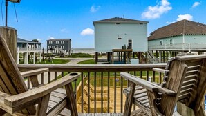 A wooden deck with chairs, overlooking a beachfront property with houses and a pier.