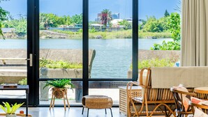 Una habitación con un ventanal grande que da a un río, mobiliario de mimbre y vistas a un paisaje urbano.