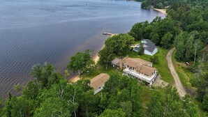 Una casa grande con un porche amplio, rodeada de un bosque frondoso y un lago.