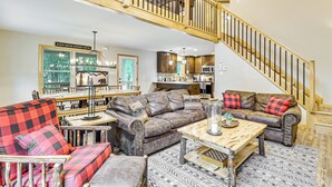 A spacious living area with a high ceiling, a wooden staircase, and a kitchen in the background. - Forest Views & Hot Tub: Poconos Cozy Cabin (Albrightsville)